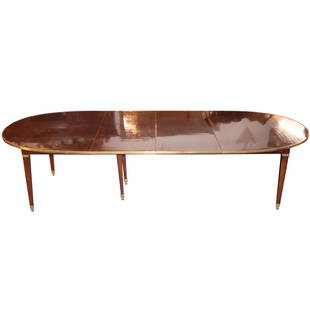 Maison Jansen Mahogany Dining Room Table: DESCRIPTION: A French Maison Jansen Dining Room Table. Featuring a mahogany and gilt bronze-mounted oval dining room table with 3 leaves and a drop down support leg. The tabletop framed apron in a bro