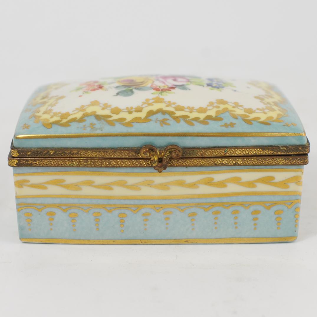 Limoges Porcelain Jewelry Box: DESCRIPTION: A Limoges hand painted porcelain jewelry box. Features painted colorful floral motifs along the lid over a blue and gilt decorated ground, the interior having a felt liner with jewelry co