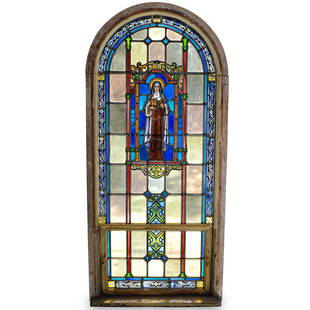 Cathedral Arched Stained Glass Window: DESCRIPTION: An arched stained glass church window. In two parts. Features colorful glass panels with a central image of The Virgin Mary holding the bible, on an arched wood frame. Originally