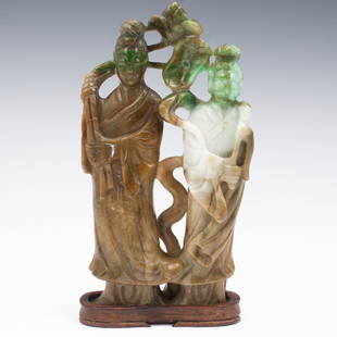 Chinese Jadeite Double Guanyin Figurine: DESCRIPTION: A Chinese carved jadeite figurine depicts a Guanyin figure holding large blooming flowers, alongside her stands a young robed apprentice. The jadeite features brown, light green and