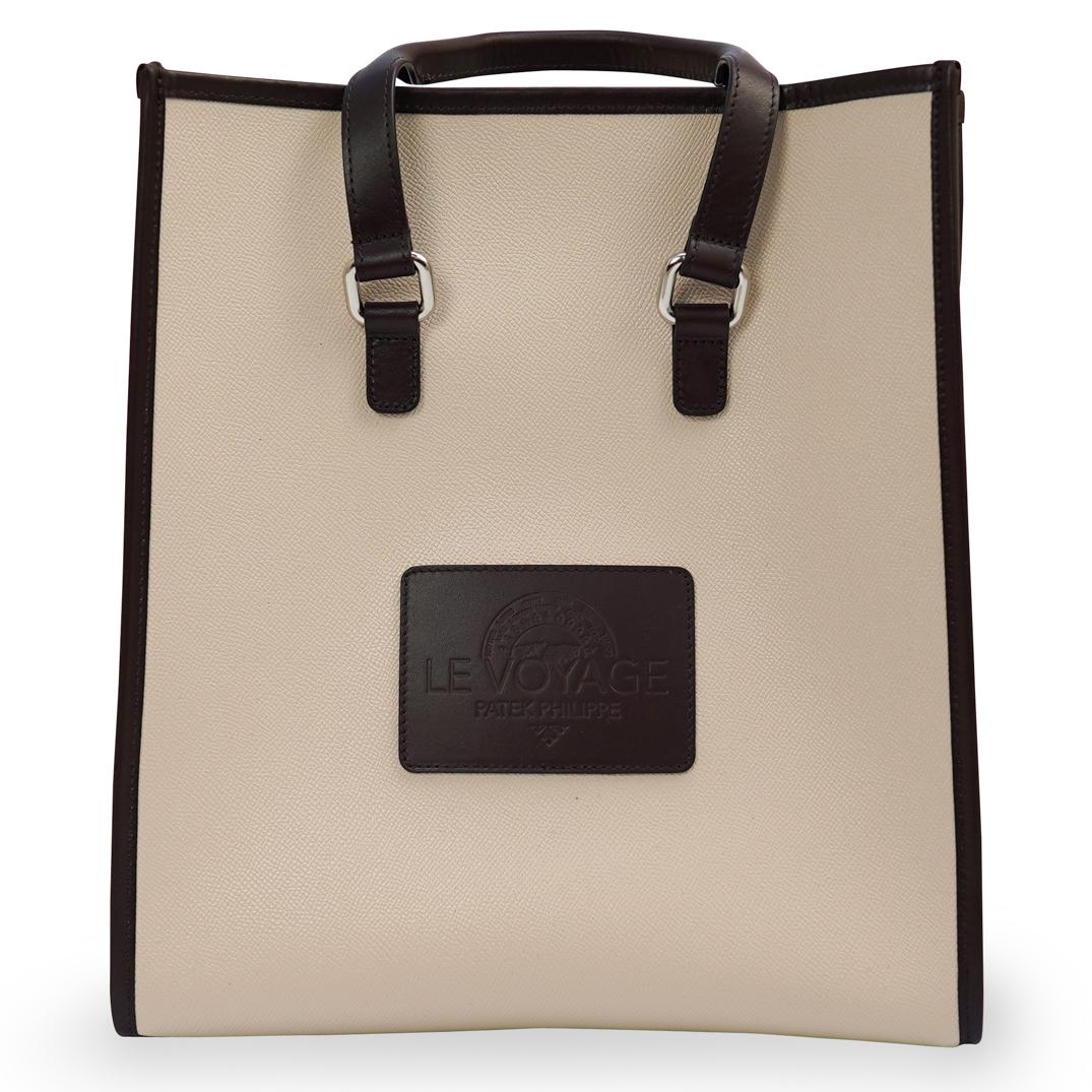 Patek Philippe "Le Voyage" Leather Tote Bag: DESCRIPTION: A Patek Phillipe Le Voyage bag, composed of beige soft leather with brown trim, stitched at the center with Le Voyage Patek Philippe logo and two handles. This bag is given to Patek Phili
