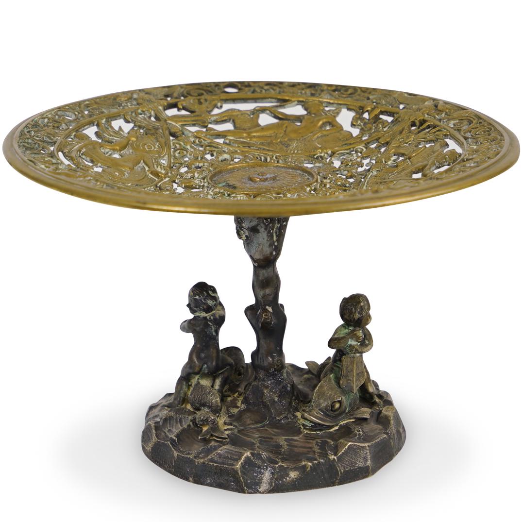 Elkington and Co. Bronze Tazza: DESCRIPTION: A Bronze Tazza by English Makers Elkington and Co. features a figural base and stem depicting two children rowing atop the backs of dolphins. The bowl of the tazza in intricately decorate