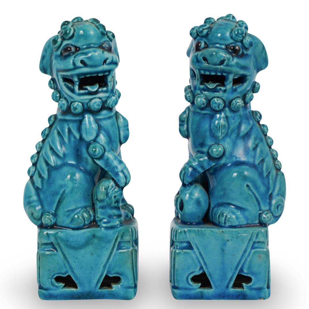 Pair of Chinese Turquoise Porcelain Foo Dogs: DESCRIPTION: Pair of Chinese porcelain foo dogs. Each are seen wearing regal saddles, and dangling objects with their paws atop beasts, and orbs. Each are finished in matching hued, turquoise glazes. 