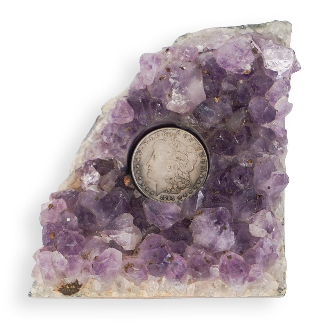 Amethyst and Silver Dollar Plaque: DESCRIPTION:A Plaque fitted with a Morgan silver dollar at the center of a Amethyst Geode. CIRCA: 20th Cent. DIMENSIONS: H: 5.5" W: 5" CONDITION: Great condition. See lot description for details on it
