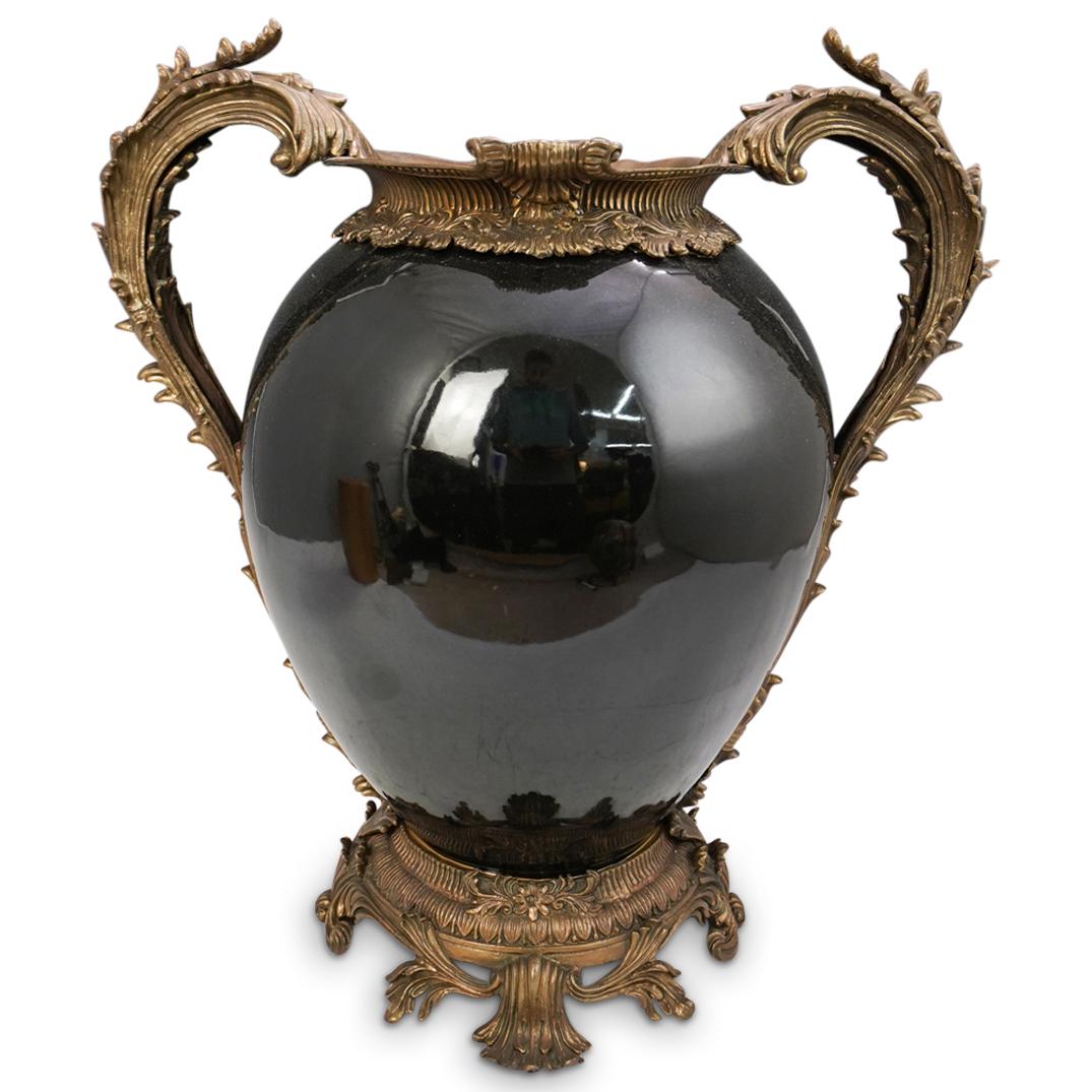 Castilian Ceramic & Bronze Urn: DESCRIPTION: A urn by Castilian composed of a porcelain body mounted with a bronze frame. Decorated in a scrolled rococo designs with two arching side handles flanking the body and a glossy glaze. Mar