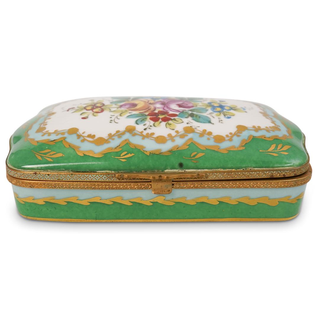 Antique Sevres Porcelain Box: DESCRIPTION: A French Sevres hand painted porcelain dresser box. Features an overall green color with floral decorations on the top lid. Opens to reveal a white interior and fitted with dore bronze li