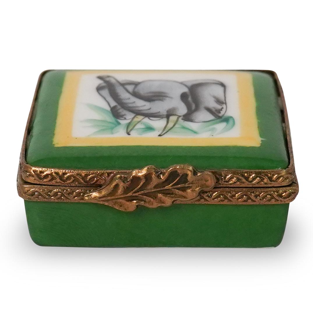 Limoges Porcelain Elephant Pill Box: DESCRIPTION: Limoges porcelain pill box adorning an elephant with tusks on the lid. The pill box adorns a green hue all around with green accents and gilt trimming. Signed "Limoges" underneath CIRCA: 