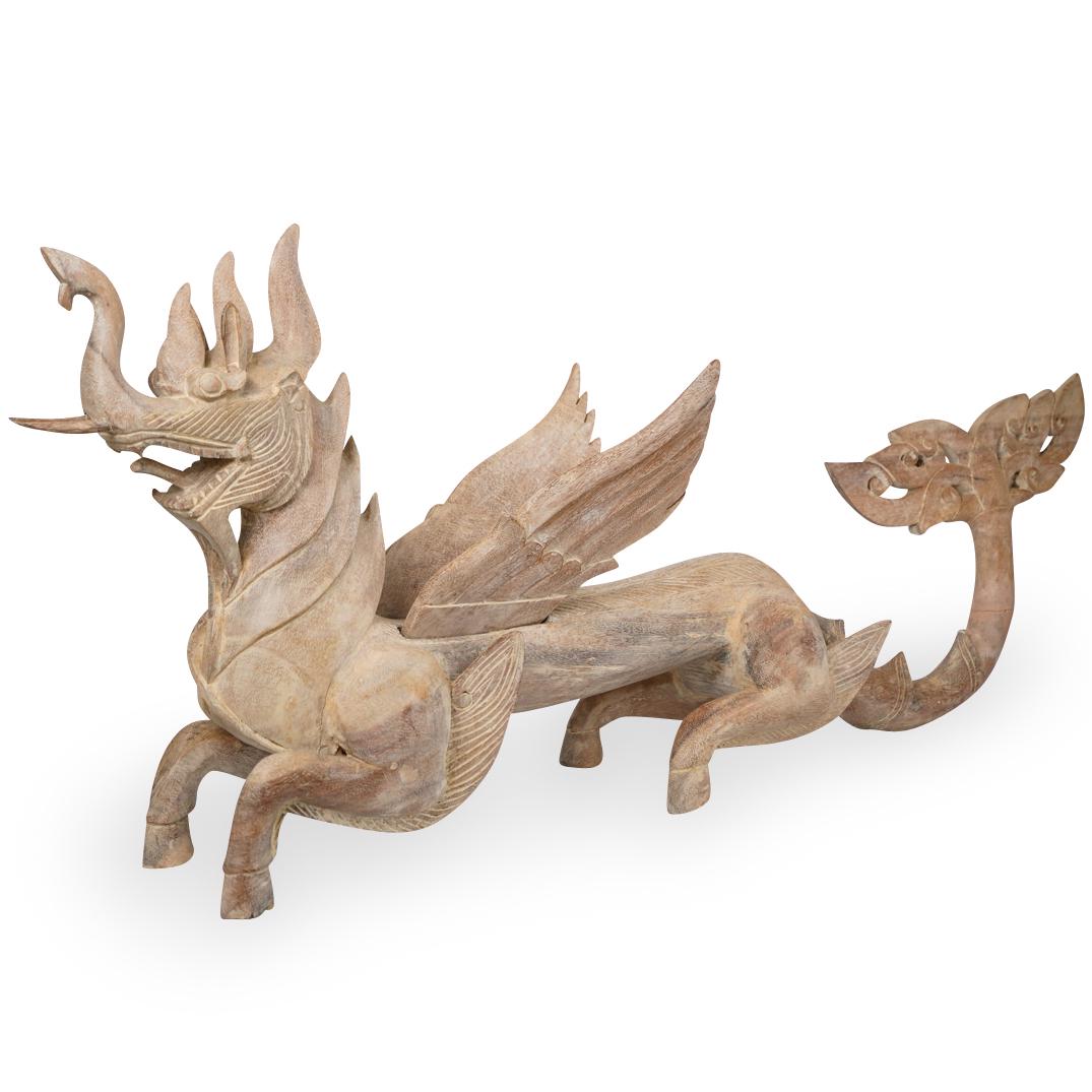 Wood Carved Balinese Dragon: DESCRIPTION: A hand carved wood Balinese dragon. Features a washed wood foundation with hooved feet, raised wings, and open work carved tail. Finished with pointed feather-like accents and open mouth.