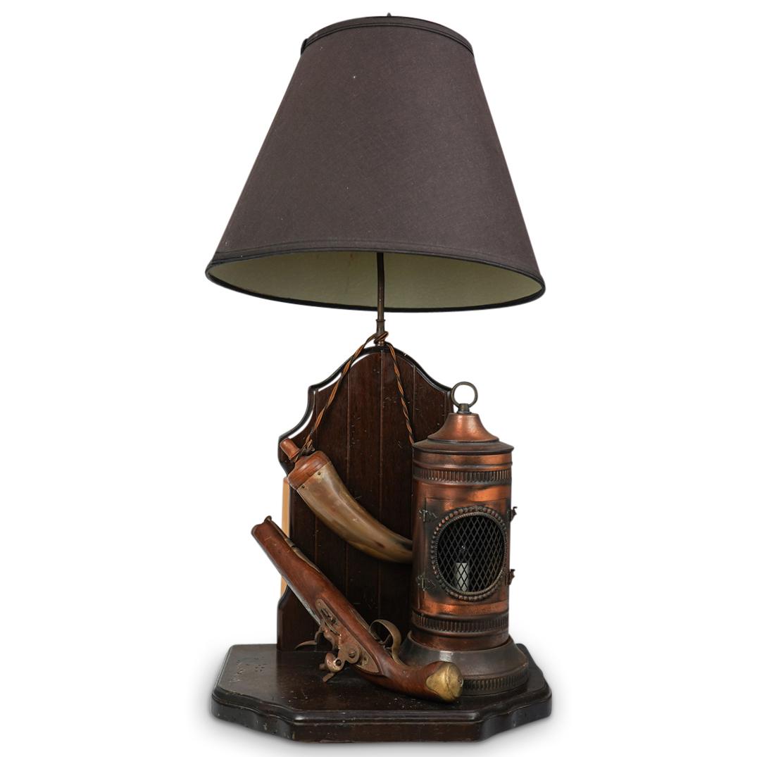 Night Watch Co. Hunting Scene Table Lamp: DESCRIPTION: A "Nightwatch Lamp Company" table lamp. Composed of a wood foundation mounted with a flintlock pistol, drinking horn, and a brass flickering candle flame lantern. Fitted with a single bul