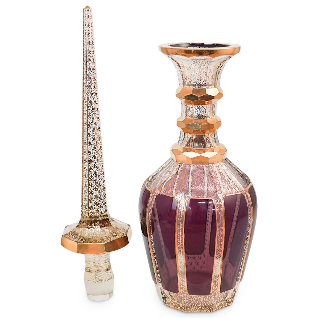 Moser Gilt Glass Decanter: DESCRIPTION: A Moser gilt glass decanter with tapered neck, flared rim, and elongated pointed stopper. Finished with abstract and floral design accents. CIRCA: 20th Cent. ORIGIN: Czech Republic DIMENS