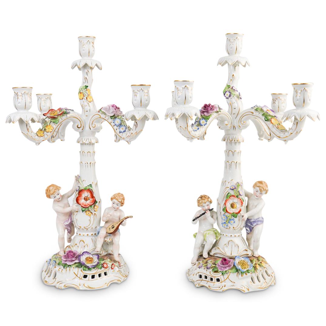 Pair Of Von Schierholz Porcelain Candelabras: DESCRIPTION: A pair of figural porcelain candelabras by "Von Schierholz". Features two nude putti figurines wrapped around the tree trunk motif center stem garnished with flowers and foliage. Further 