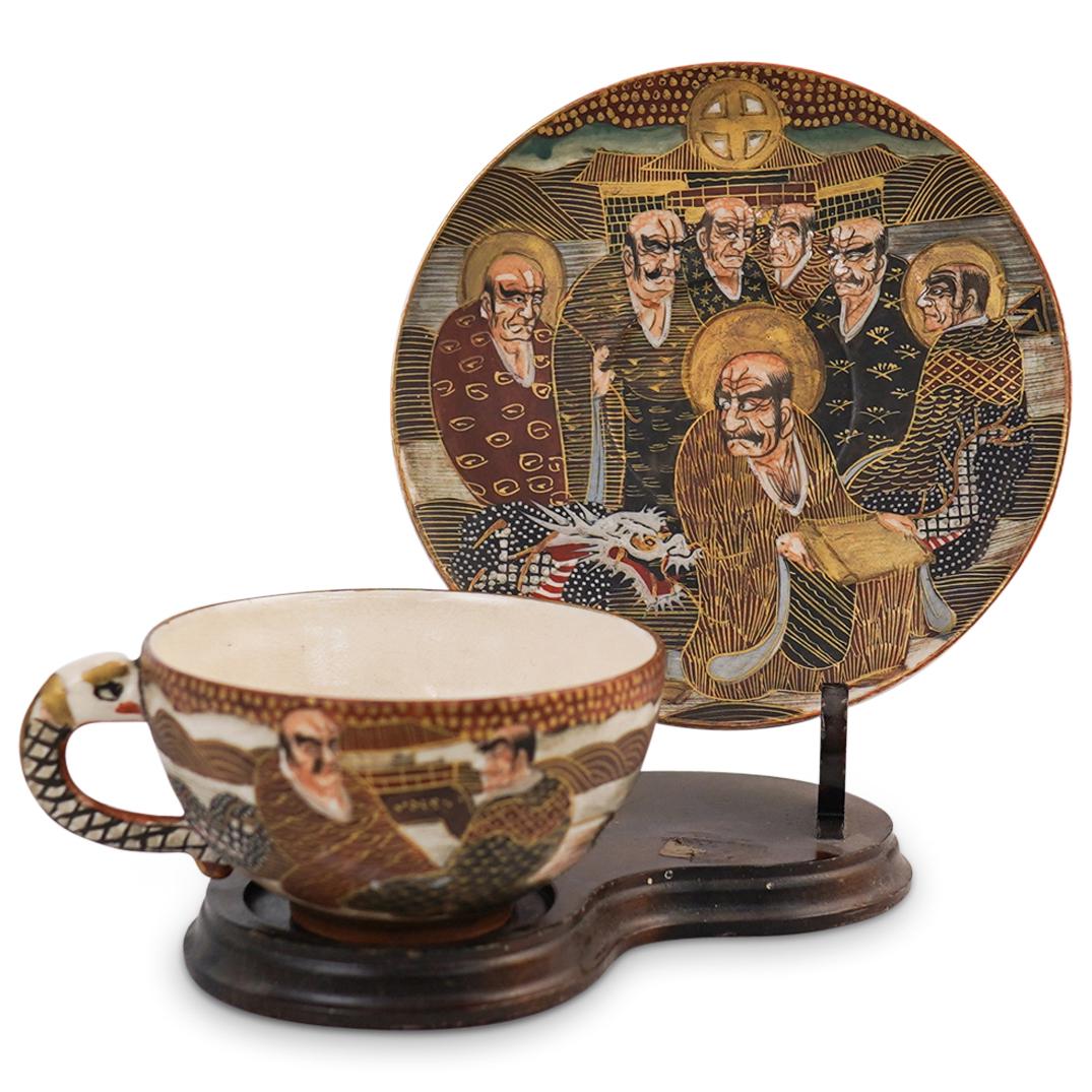 Antique Japanese Satsuma Tea Cup: DESCRIPTION: An antique Japanese Satsuma tea cup with dish. Features hand painted depictions of regal Japanese figures with dragon patterns and spiraling designs. Marked with Japanese characters under