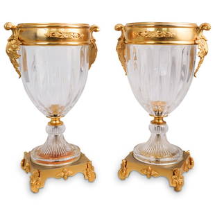 Pair Of Crystal & Dore Bronze Vases: DESCRIPTION: A pair of crystal cut dore bronze mounted vases. Each vase features double gilt scrolling handles with a tapered stem crystal body and ornate acanthus leaf accent, footed base. CIRCA: