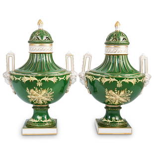 Pair Of Dresden Porcelain Urns: DESCRIPTION: A pair of Dresden porcelain urns with double figural adorned handles and hand painted center floral motifs. Each urn finished with vibrant green and ornate gilt accented colorations. Comp