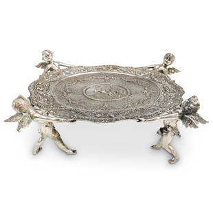 German 800 Silver Figural Footed Platter: DESCRIPTION: A German Silver Figural footed platter features four putti angels, one on each corner supporting a beautifully decorated repousse reticulated center platter. The center garnished by