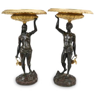 Antique Bronze Blackamoor Tazzas: DESCRIPTION: A pair of antique bronze patinated Blackamoor Tazzas, featuring male and female figures draped in loincloths and carrying ewers. The stem supports an ornately decorated gilt bronze bowl,