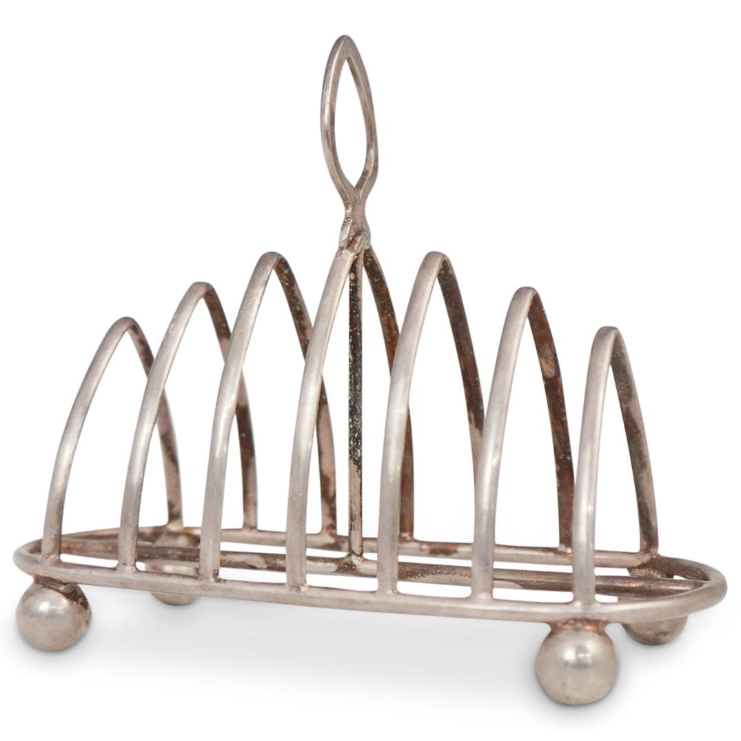 English Sterling Toast Holder: DESCRIPTION: An English sterling silver toast holder with arched holding arms, open spade finial, and a sphere footed base. Hallmarked. CIRCA: Early 20th Cent. ORIGIN: England DIMENSIONS: H: 5.5" x D: