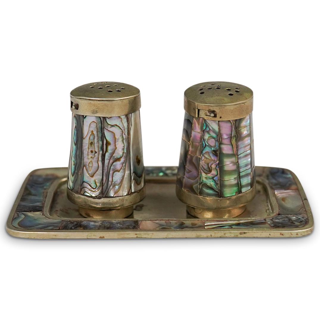 Mexican Abalone and Brass Shaker Set: DESCRIPTION: A set of salt and pepper shakers feature a brass foundation inlaid with abalone, unmarked. CIRCA: Mid 20th Cent. ORIGIN: Mexico DIMENSIONS: H: 2" (Tray) L: 4" CONDITION: Great condition.