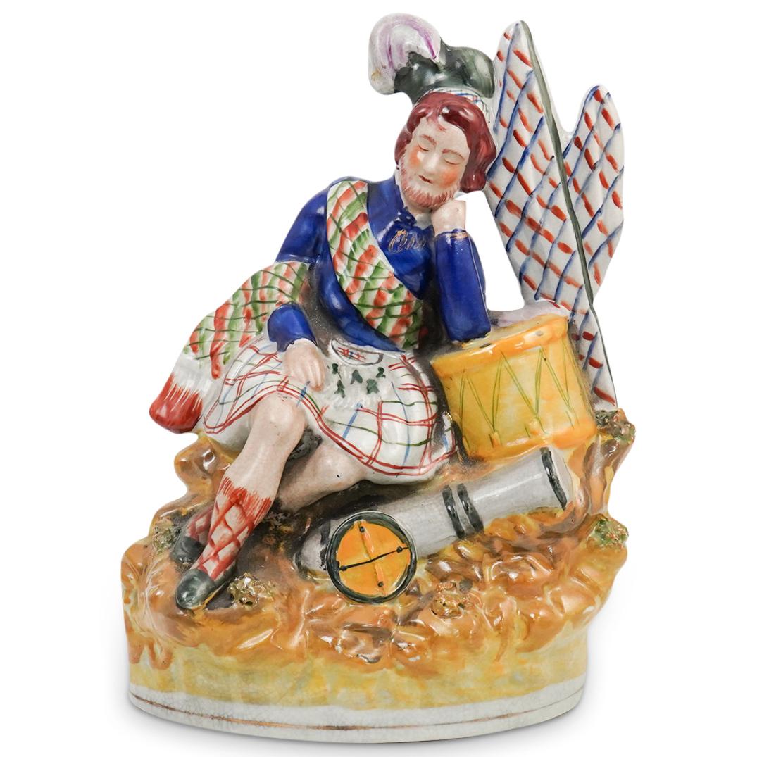 Victorian Staffordshire Porcelain Figurine: DESCRIPTION: Victorian Staffordshire Porcelain Figurine. This is a multicolor glazed porcelain Staffordshire figure of a sitting man in a Scottish kilt, in a resting position with his head resting on 