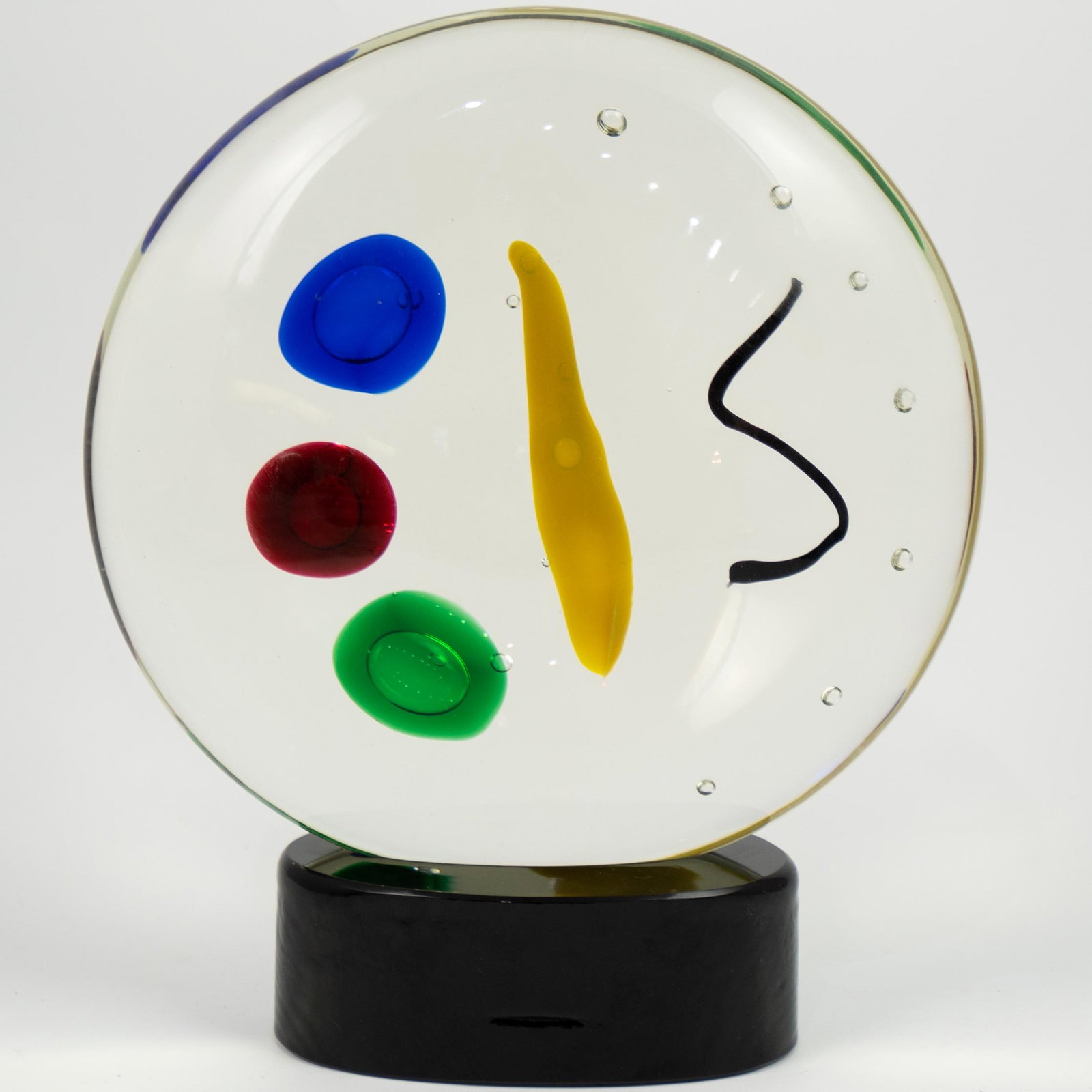 Atelier Oball Murano Glass Sculpture: DESCRIPTION: An Atelier Oball Murano glass sculpture. Features a clear glass, circular form foundation with interior spotted accents in blue, red, gree, yellow, and black tones. Finished with an oval 