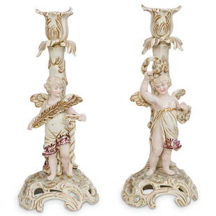 (2 Pc) Antique German Porcelain Putti Candlesticks: DESCRIPTION: (2 Pc) An antique German porcelain figural putti candlesticks depicting a winged cherub angel holding a sword and feather the first one, and a laurel wreath. Both figurines are marked on