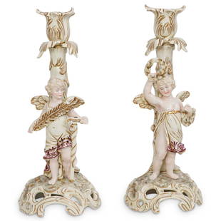 (2 Pc) Antique German Porcelain Putti Candlesticks: DESCRIPTION: (2 Pc) An antique German porcelain figural putti candlesticks depicting a winged cherub angel holding a sword and feather the first one, and a laurel wreath. Both figurines are marked on