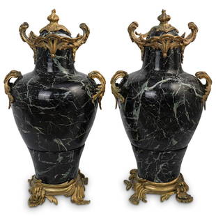 Pair Of Marble & Gilt Bronze Urns: DESCRIPTION: A pair of black veined marble and gilt bronze mounted urns. Features acanthus leaf footed bases with double leaf motif handles. Finished with scrolling floral decorated tops and torche fi