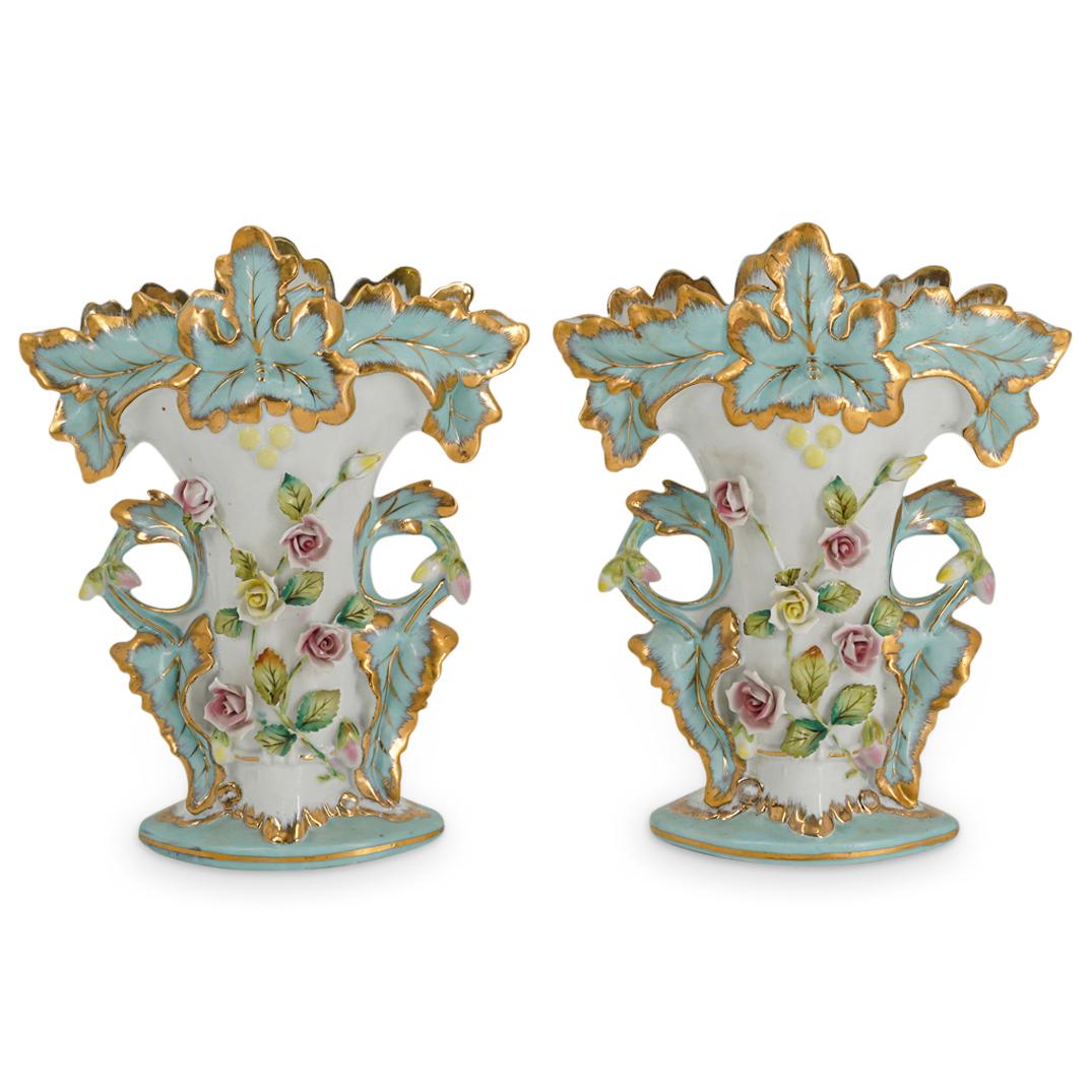 (2 pc) Floral Porcelain Vases: DESCRIPTION: Two porcelain vases with textured floral motif against white background. Base and lip have light blue leaf pattern with gilt edges. Handles have similar pattern with buds on either side.