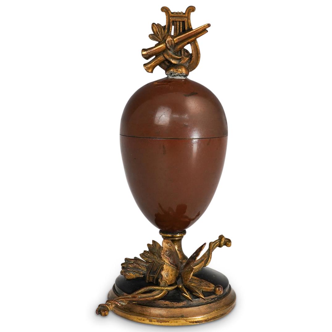 After Louis Auguste Moreau (1855-1919) Bronze Egg Box: DESCRIPTION: An after Louis Auguste Moreau bronze egg potpourri box. Features a bronze foundation with enamel exterior, decorated with a gilt bronze bow and butterfly accent and finished with a harp a