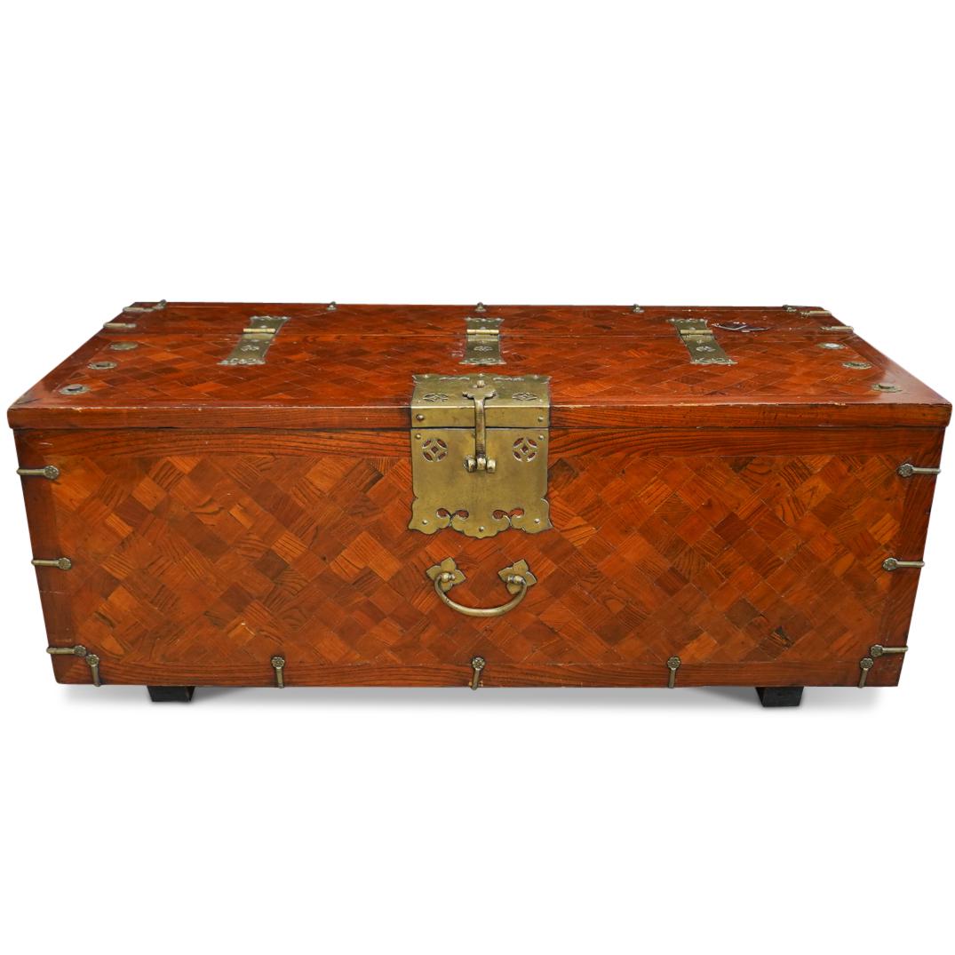 Vintage Marquetry Wooden Trunk: DESCRIPTION: A Vintage wooden trunk decorated with a Marquetry checkerboard pattern, further accented by brass medallions and hardware. Flanking each side are brass handles, the top opens vertically b