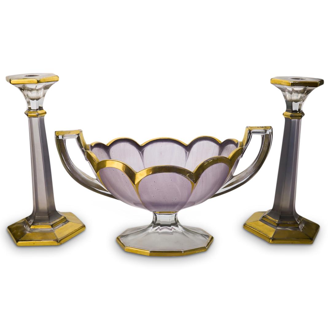 Art Deco Amethyst Glass Garniture Set: DESCRIPTION: Art Deco Amethyst Garniture Set composed of two candlesticks and a footed centerbowl. Features a lavender matte hue and embellished with gilded trim.CIRCA: 1930'sORIGIN: USADIMENSIONS:H:9