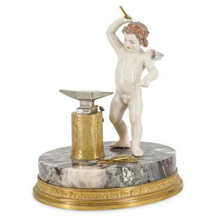 French Putto Blacksmith Porcelain Figurine: DESCRIPTION: A French porcelain figurine of a putto blacksmith hammering metal atop an oval, veined marble base embellished with a gilt metal rim. CIRCA: Early 20th Century. ORIGIN: France. DIMENSIONS