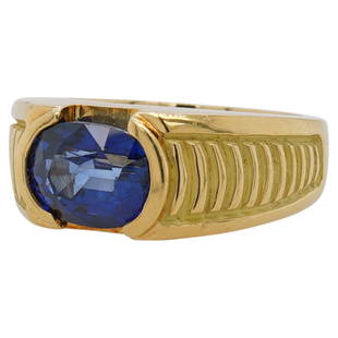 18k Gold and Sapphire Ring: DESCRIPTION: A 18k yellow gold ring centered by an approx. 2.5ct oval cut Sapphire in a bezel setting, accented along the shoulders with graduating textured design. Stamped along the inner band