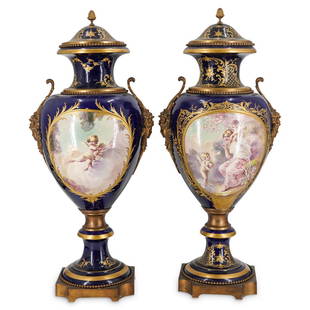 Pair of Antique Cobalt Blue Sevres Urns: DESCRIPTION: A pair of cobalt blue French Sevres urns, featuring porcelain foundations mounted with double figural gilt bronze handles, beaded trims, and footed bases. Further decorated with hand