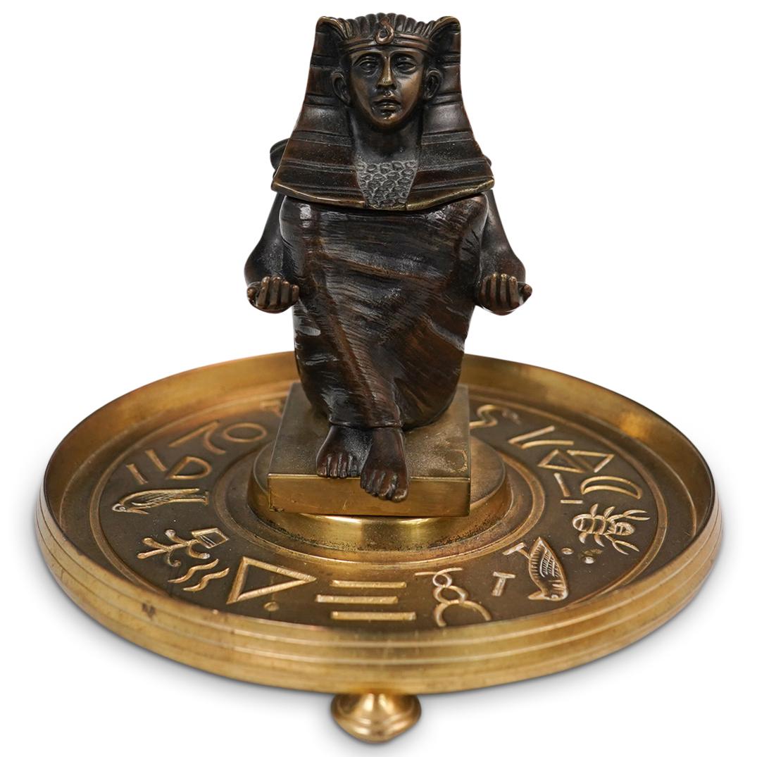 Egyptian Revival Bronze Pharaoh Inkwell: DESCRIPTION: An Egyptian Inkwell made of bronze and brass depicting a Pharaoh on a sitting pose with extending offering arms. The bronze pharaoh sits on a brass three legged plate base further decorat