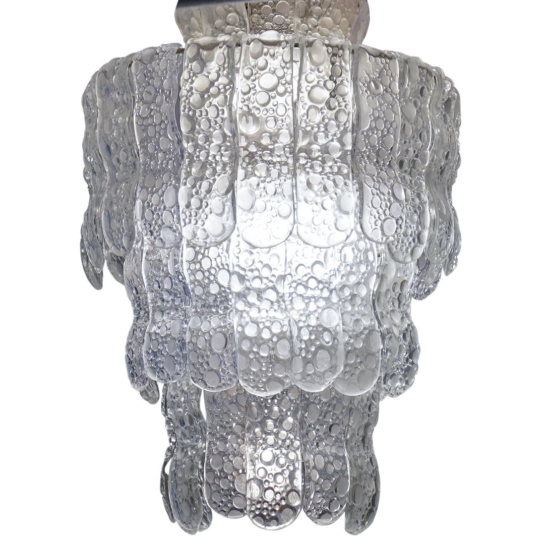 Vintage Murano Textured Glass Tiered Chandelier: DESCRIPTION: A Mid-Century Murano glass three-tiered chandelier with pebble textured hanging glass shades. Fixture composed of metal with (9) lightbulb outlets. Stamped: "Made In Italy" at fixture. CI