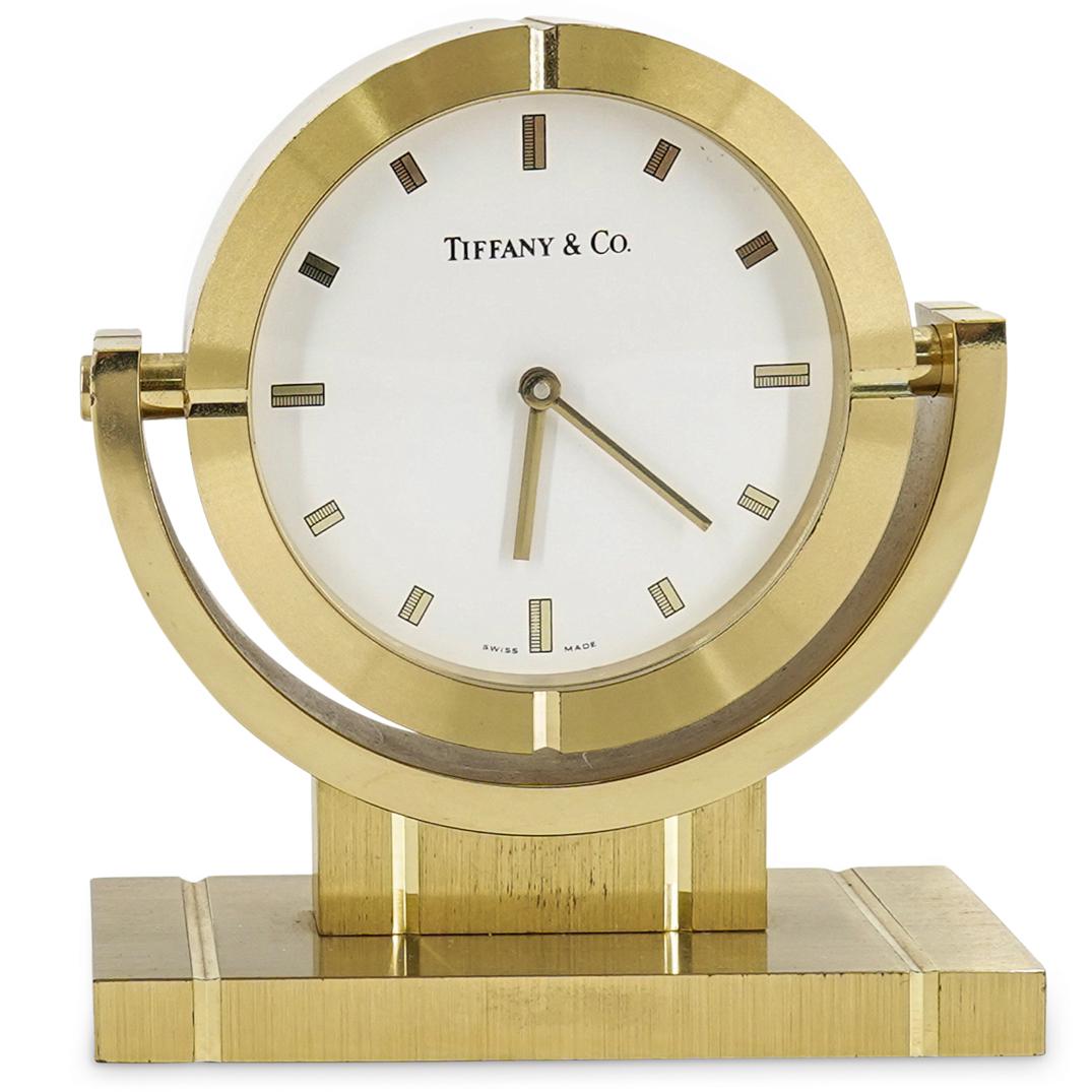 Tiffany & Co. Travel Alarm Clock: DESCRIPTION: A Tiffany & Co. travel alarm clock. Designed with a classic design and quartz technology, and finished with a polished brass case. With a white dial and black arabic numerals. Includes a 