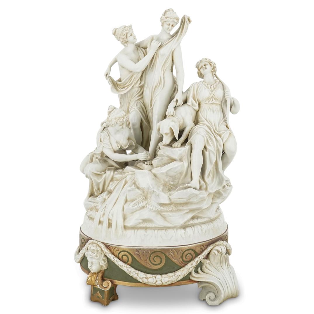 Porcelain Sculpture Of Artemis With Oreads In Attendance: DESCRIPTION: White porcelain sculpture depicting a crowned Artemis attended by oreads and a hound by a rocky stream. Piece features a green and gilt base decorated with foliage-form feet, putto faces,