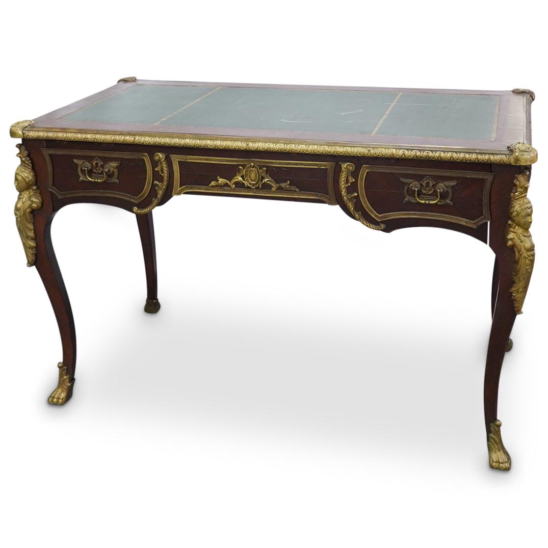 Antique French Wood and Bronze Desk: DESCRIPTION: Wooden desk featuring a green leather desktop with gilt, foliage patterned borders. Legs, corners, and sides are decorated with bronze trimmings including bronze female busts on the legs 