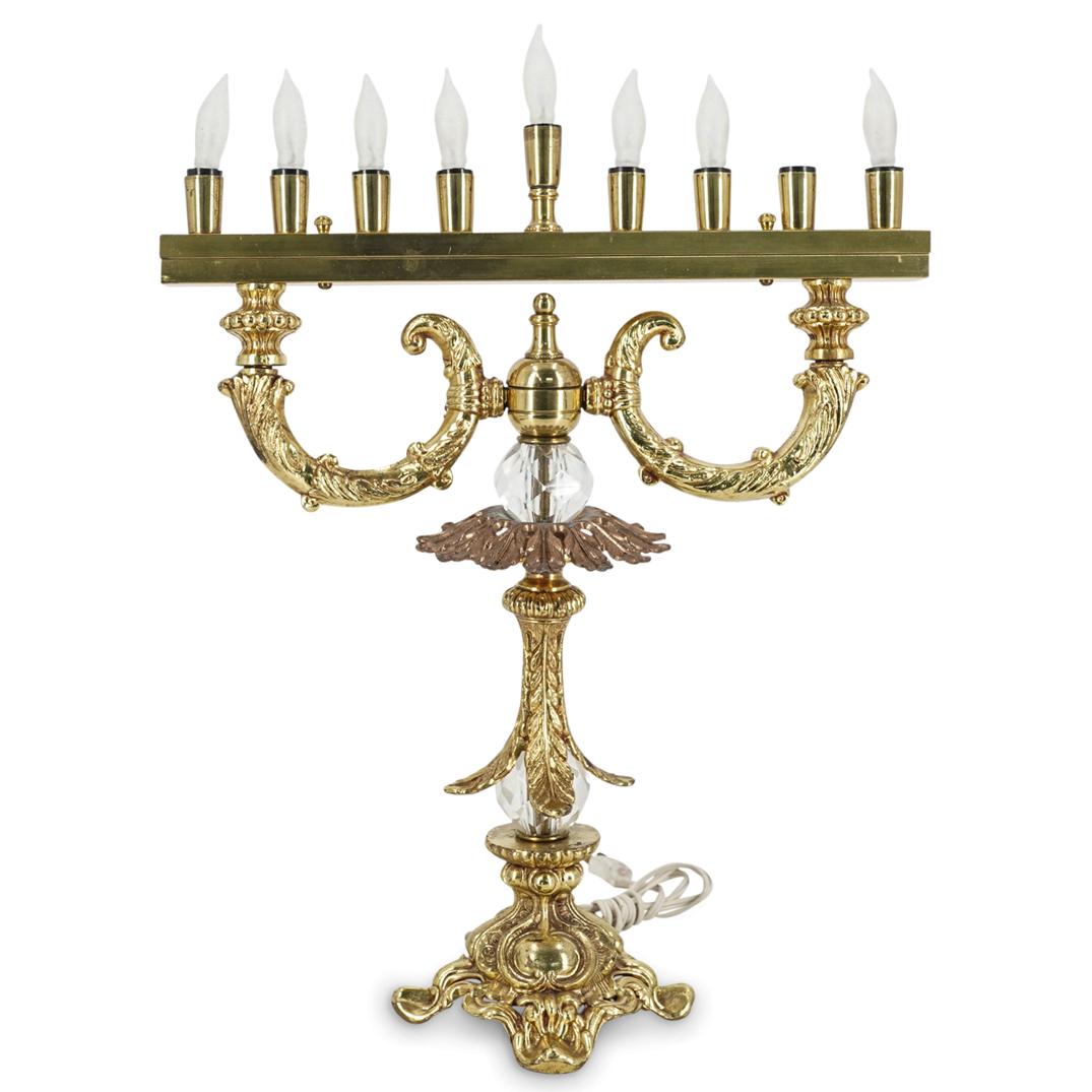 Gilt Metal And Glass Menorah: DESCRIPTION: Gilt metal electric menorah featuring nine sockets, foliage designs throughout, and faceted glass accents on the stem. Tested and fully functional CIRCA: 20th Century ORIGIN: USA DIMENSIO