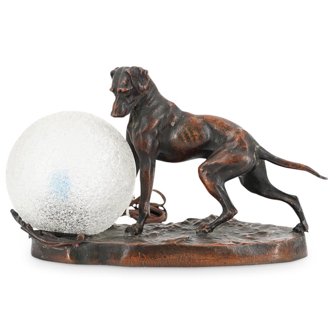 Art Deco Spelter Dog Lamp: DESCRIPTION: Antique art deco sculptural electric lamp composed of spelter and depicting a dog looking down at the light with a web sphere glass shade. CIRCA: Early to Mid 20th Century ORIGIN: USA DIM