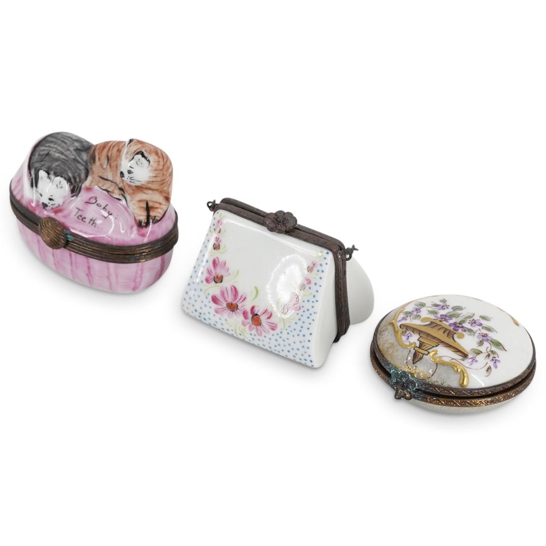 (3 Pc) Limoges Hand Painted Pill Boxes: DESCRIPTION: Three hinged lid, hand-painted Limoges pill boxes: one purse form with a chain-link handle, one decorated with violets on a gilt bracket, and one with two cats in a cradle marked "Baby Te