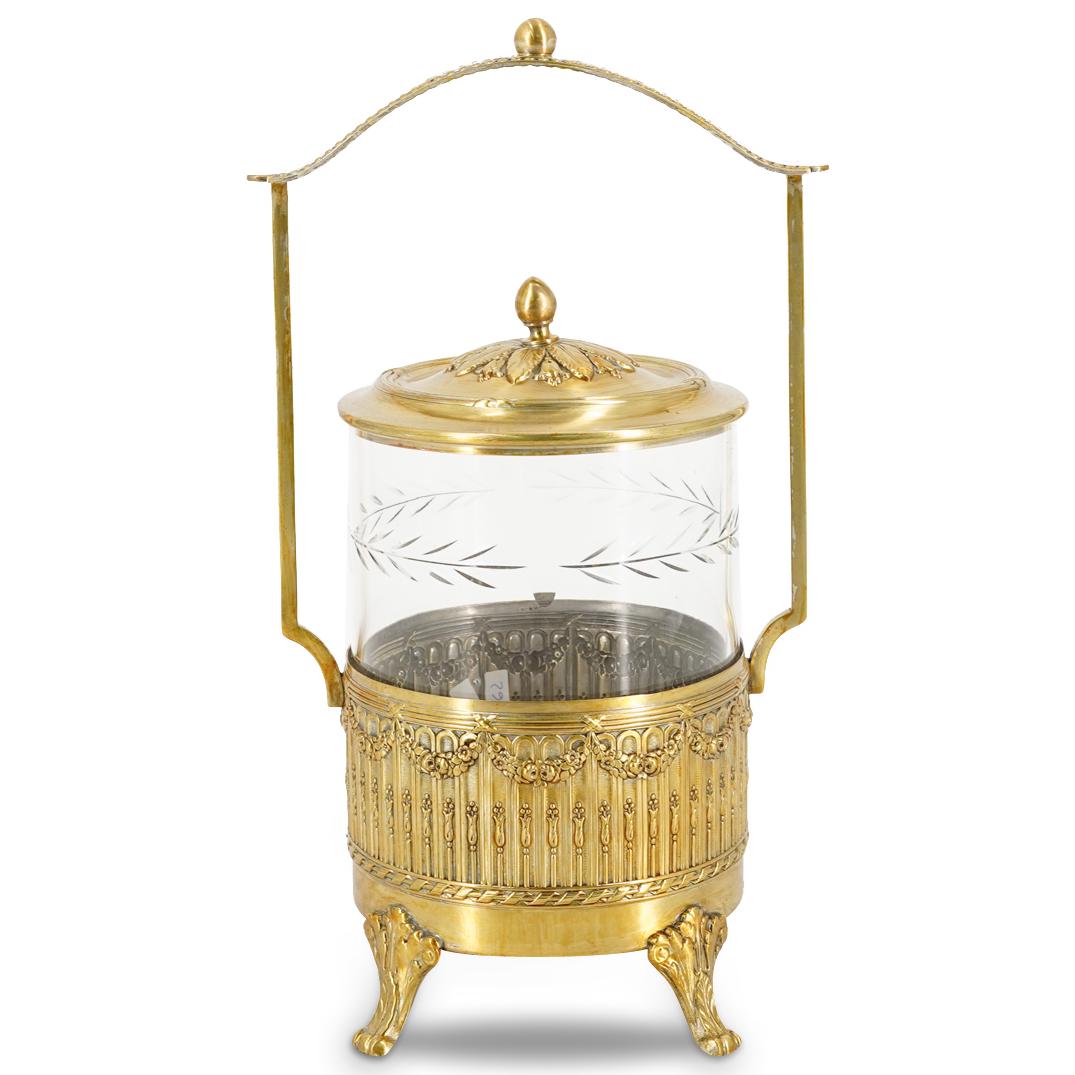 Mixed Metal And Glass Pickle Castor: DESCRIPTION: A mixed metal and glass pickle castor. A round base with a raised apron holds the glass pickle jar. The apron of the base has repousse geometric and floral garlands designs. The clear gla