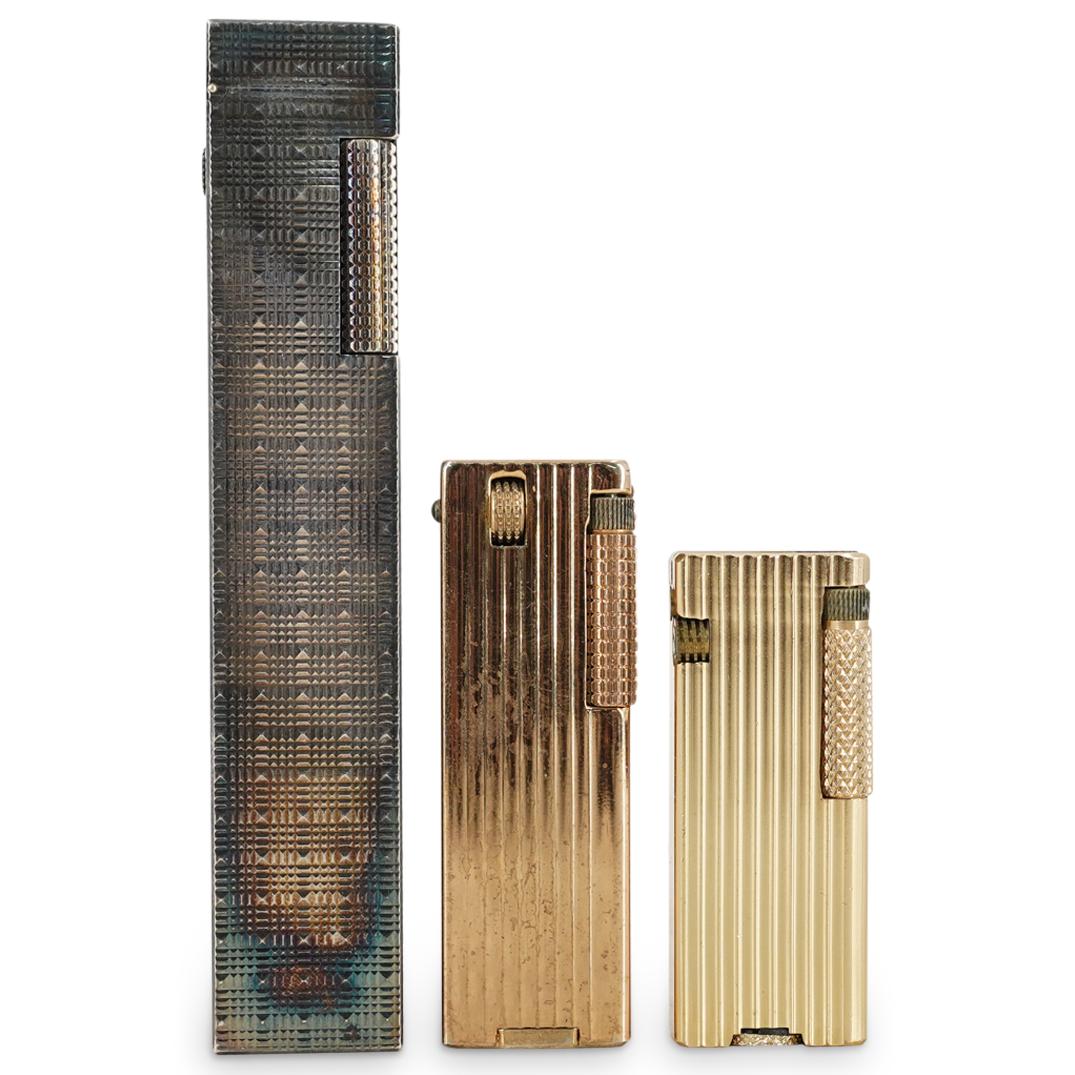 (3 Pc) Pocket Lighters Grouping Set: DESCRIPTION: (3 Pc) A pocket lighter grouping set, including: one (1) Penguin Cygnus pocket lighter with corrugated ribbed body and gold tone finish. Marked "Penguin Cygnus"; one (1) Cupid pocket ligh