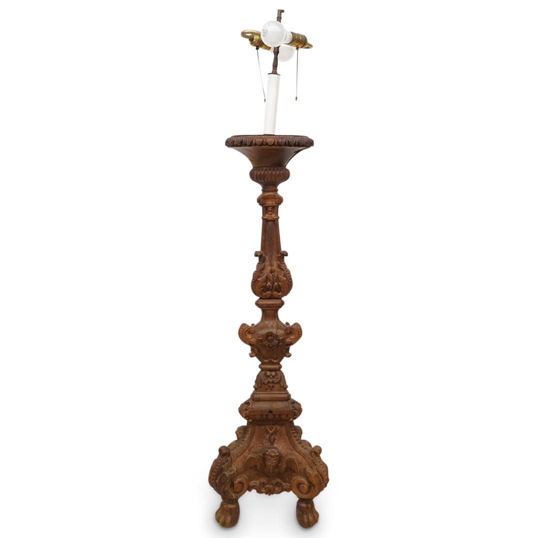 Antique Italian Baroque Carved Wood Altar Stick Lamp: DESCRIPTION: Antique Italian wood alterstick lamp featuring a tri-footed design of paws, carved symmetrical foliate scrollwork throughout and depictions of masks at the three lower faces. (Aisle 1, Ba