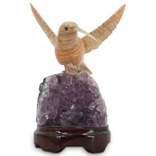 Amethyst and Semi Precious Stone Hummingbird: DESCRIPTION: A Humming bird sculpture comprised of Fluorite beak and beige stone body, seated atop an Amethyst Quartz specimen, further fitted atop a wooden base. CIRCA: 21st Cent. ORIGIN: Brazil DIME