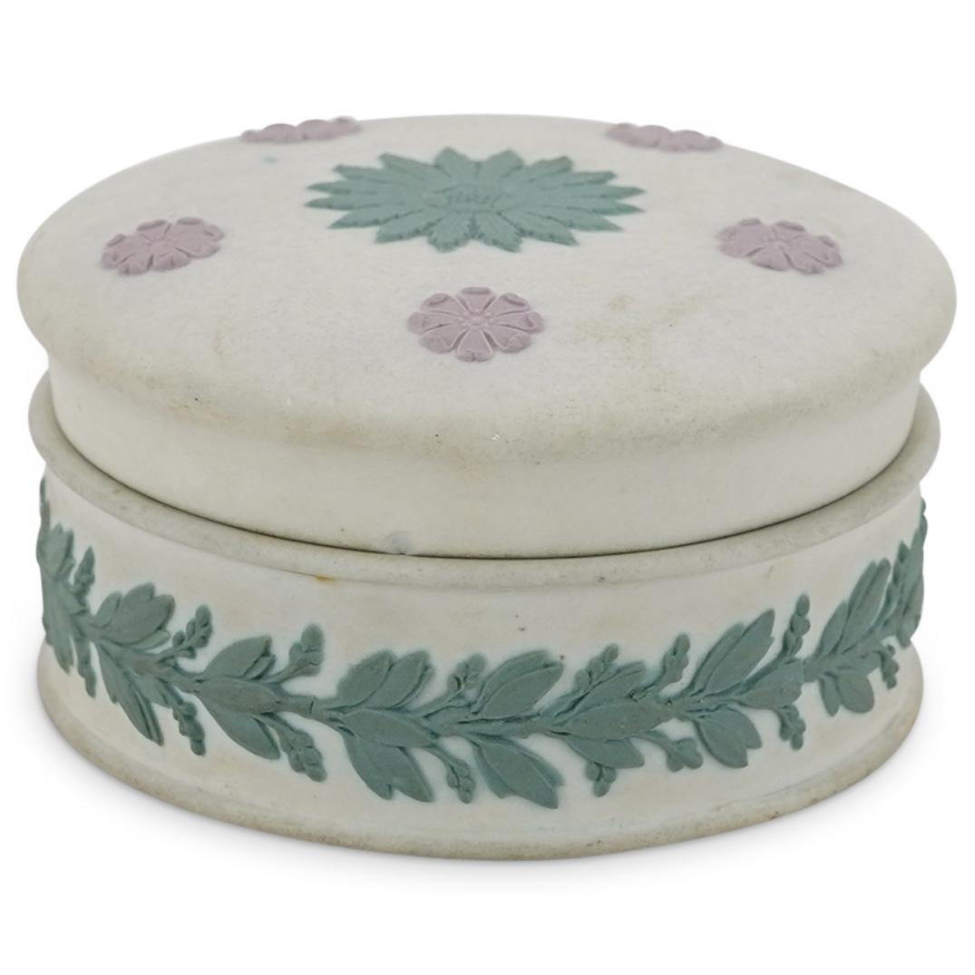 Wedgwood Jasperware Round Porcelain Trinket Box: DESCRIPTION: Wedgwood jasperware porcelain trinket box featuring a removable lid decorated with pink and green floral designs in relief against an off-white background. Embellished on sides of base wi