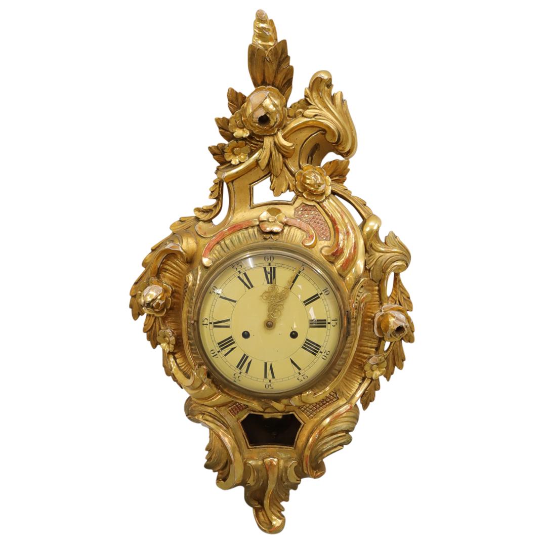Antique Swedish Giltwood Cartel Clock: DESCRIPTION: Antique Swedish parcel gilt wood cartel pendulum clock featuring carved flower and scrolling foliage depictions in high relief, an off white face with black roman numerals and gold toned