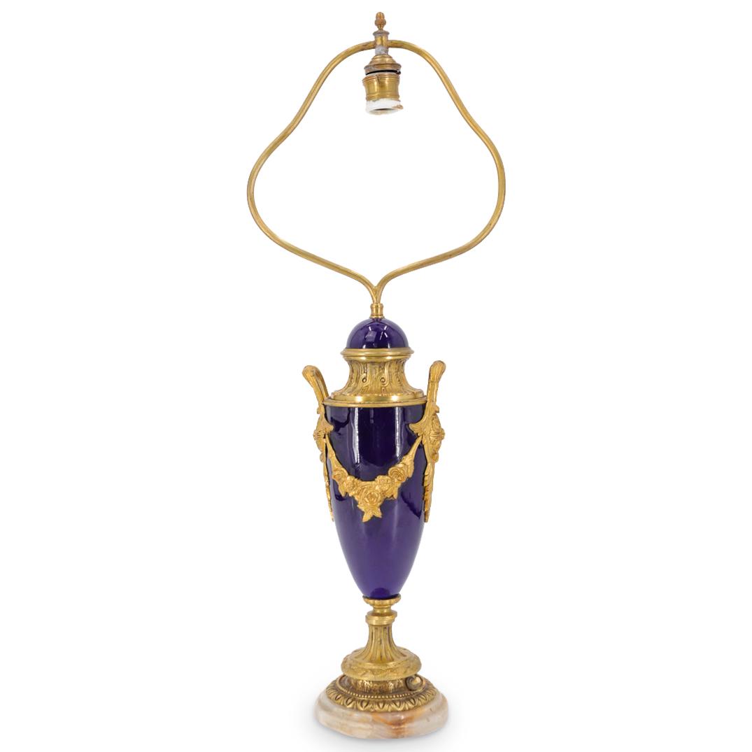 Sevres Style Bronze And Porcelain Lamp: DESCRIPTION: Sevres-style, single socket lamp featuring a blue porcelain body adorned with gilt bronze, foliage form trimmings and handles, and a gilt bronze harp crowned with an acorn finial. Piece i
