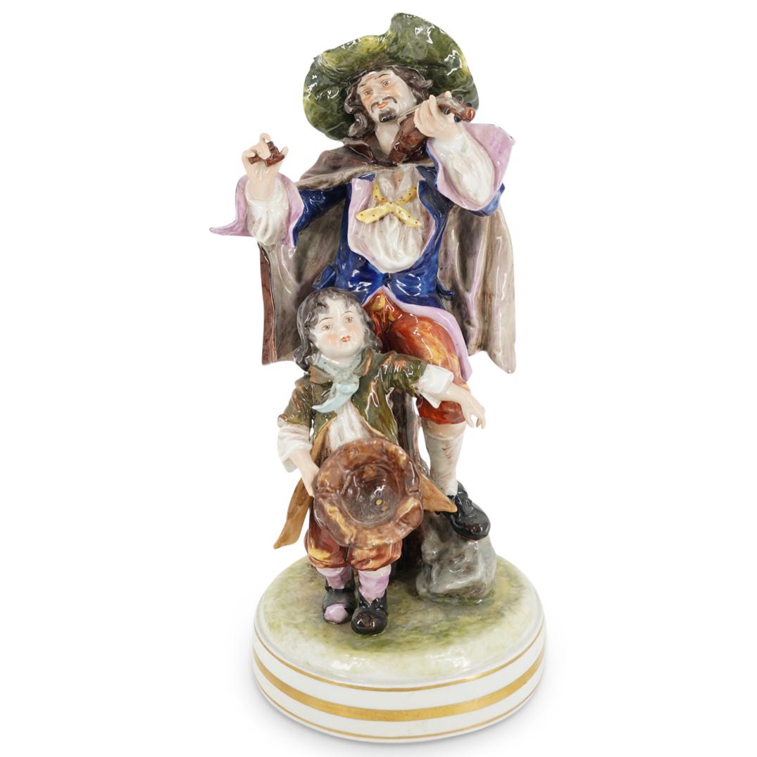 German Porcelain Figural Group: DESCRIPTION: German polychrome Porcelain figural group depicting a man with fiddle and child begging for money, stamped: "Made In Germany" CIRCA: 20th Century ORIGIN: Germany DIMENSIONS: H: 13.5" x D:
